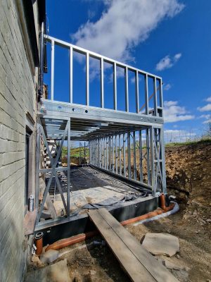 light gauge steel frame home extension under construction showing precise steel wall framing connected to existing house